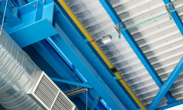 Spiral ductwork and an air handling unit below the steel ceiling of an industrial plant